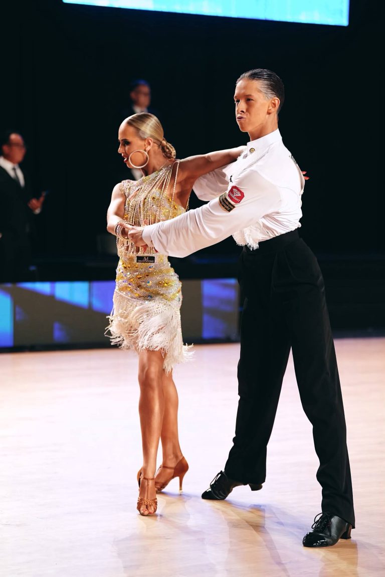 A dance couple in a gold and white Latin outfit on stage